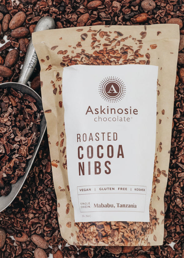 Bag of Askinosie chocolate roasted cocoa nibs with a scoop of nibs on a white background